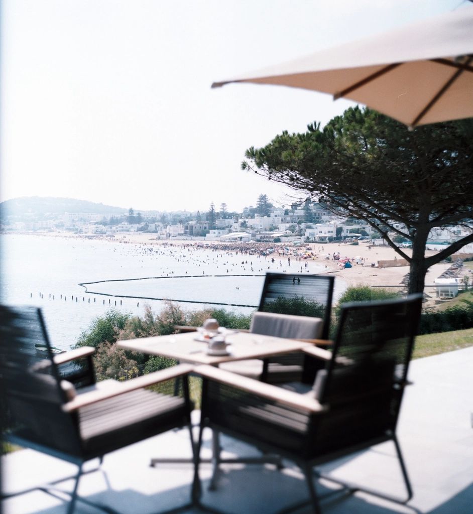 Une table de terrasse sous un parasol, l'eau en contrebas